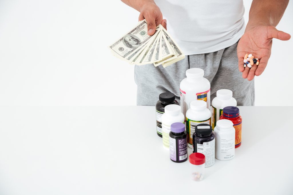 cropped image of young sportsman holding vitamins and money.