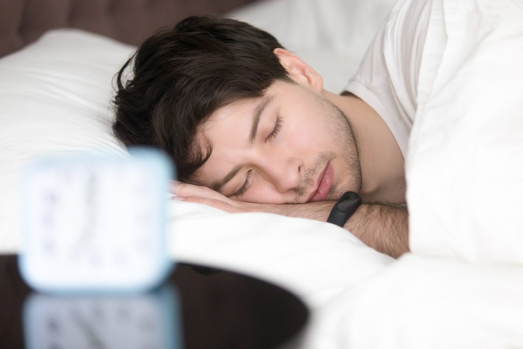 young man sleeping next to alarm clock wearing smart wristband